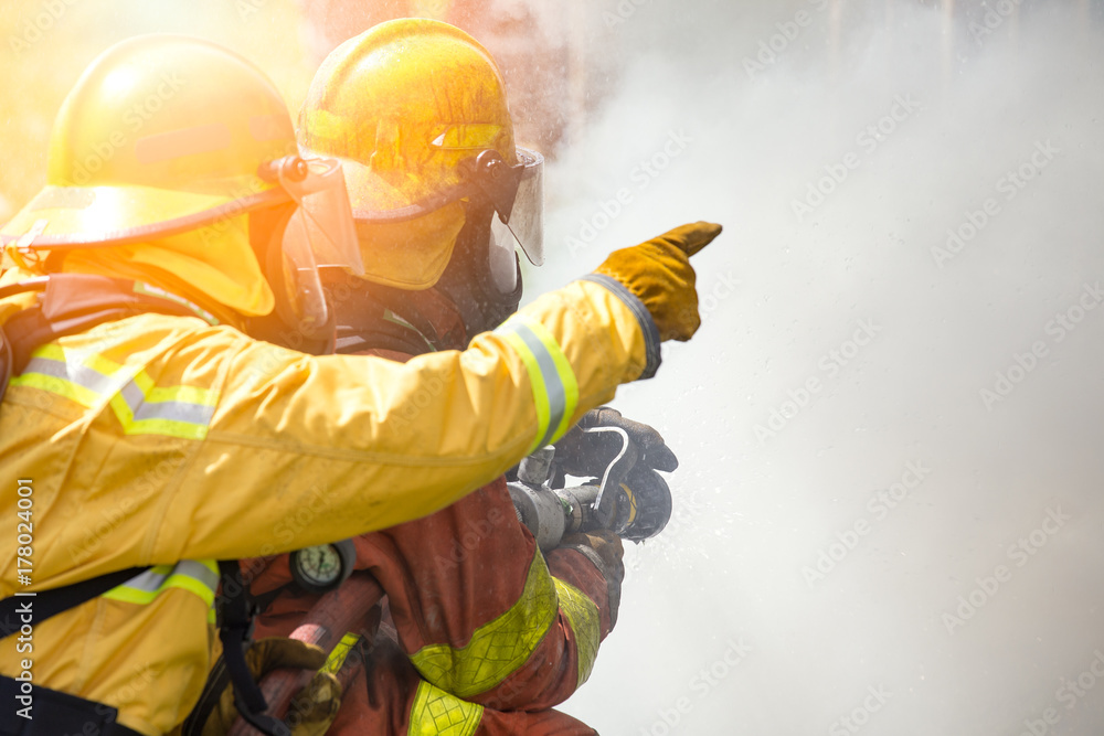 Fototapeta premium two firefighters water spray by high pressure nozzle to fire surround by smoke with flare and copy space