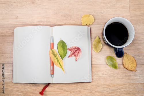 Autumn background with a cup of warming coffee, that stands on a wooden table and decorated with autumn leaves