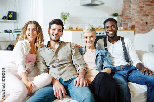 Slika na platnu Two young restful couples sitting on sofa while gathering after work or on weeke