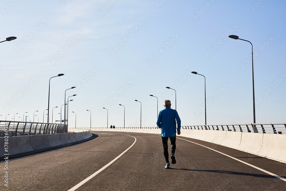 Back view of unrecognizable senior runner having intensive workout outdoors, cloudless blue sky on background Back view of unrecognizable senior runner having intensive workout outdoors, cloudless blue sky on background