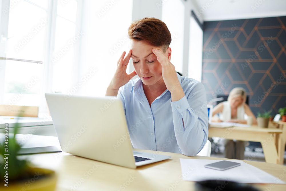 Fototapeta premium Tired or pensive woman sitting in front of laptop and preparing for report