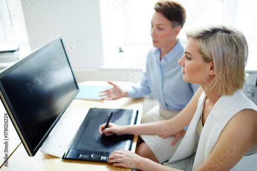 Young designer listening to her colleague advice while retouching images in front of computer