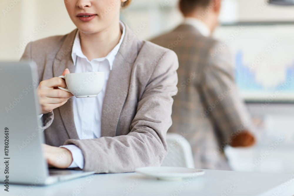 Busy female with cup of drink networking in front of laptop Busy female with cup of drink networking in front of laptop