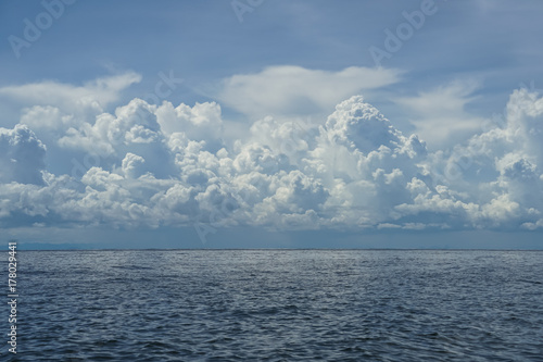 Dramatic scene of powerful free form white cloud, shades of blue sky background and deep blue sea with ocean water ripple