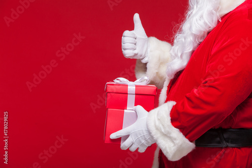 christmas Photo of Santa Claus gloved hand with red giftbox. thumb up