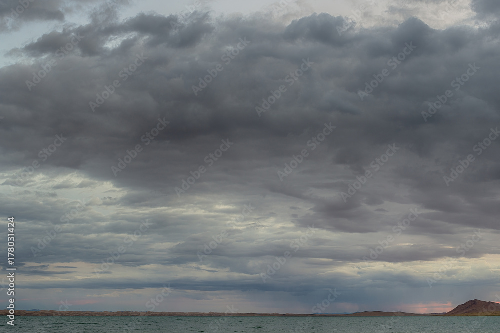sunbeams reflecting on mirror water surface of sea with dark fluffy clouds on sky 
