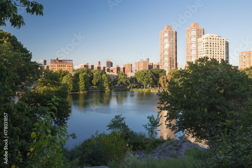 Landscape of park pond with modern building with skyscrapers far away on background reflected in water