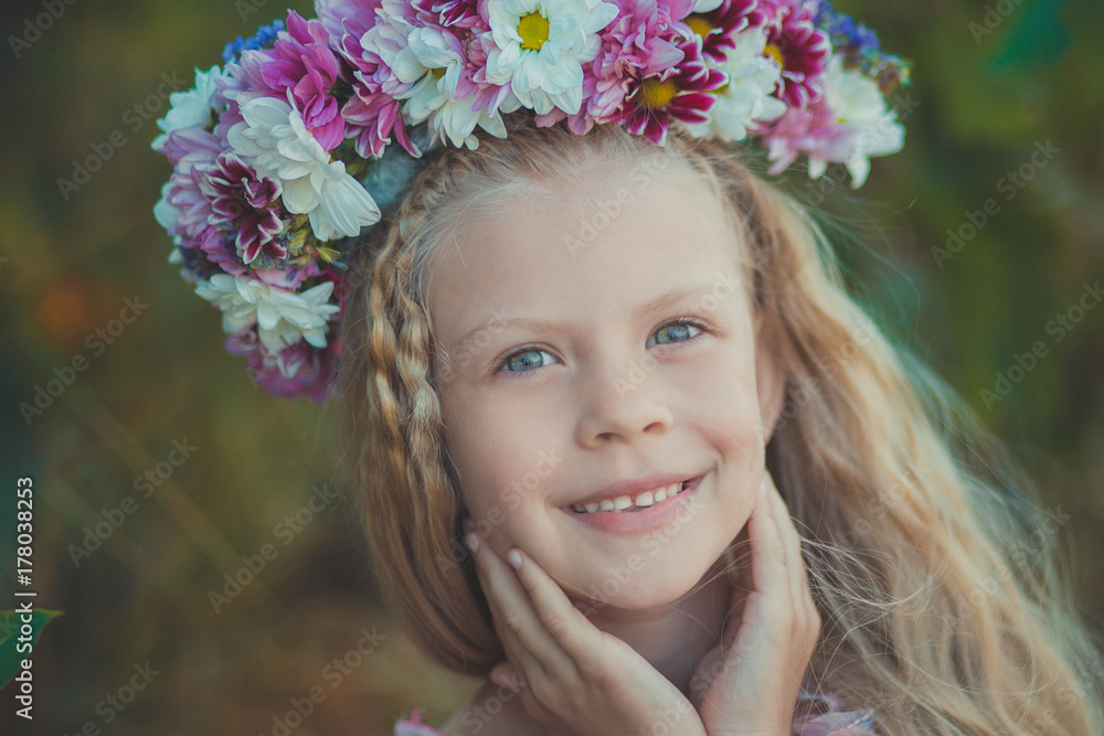 Cute blond girl with blue eyes close portrait wearing wild flowers wreath on top head smiling and looking to camera with eyes full of love joy and life. Cute blond girl with blue eyes close portrait wearing wild flowers wreath on top head smiling and looking to camera with eyes full of love joy and life.