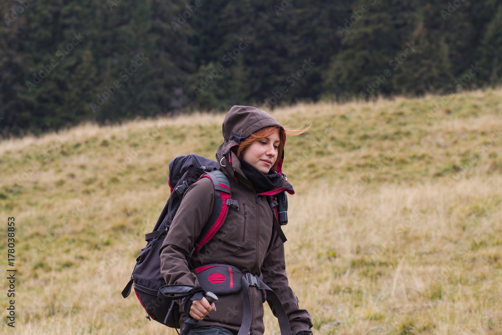 Female hiker with backpack walking on the mountains roads, autumn forest background 