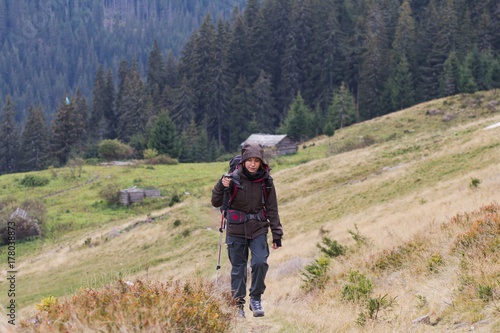 Female hiker with backpack walking on the mountains roads, autumn forest background 