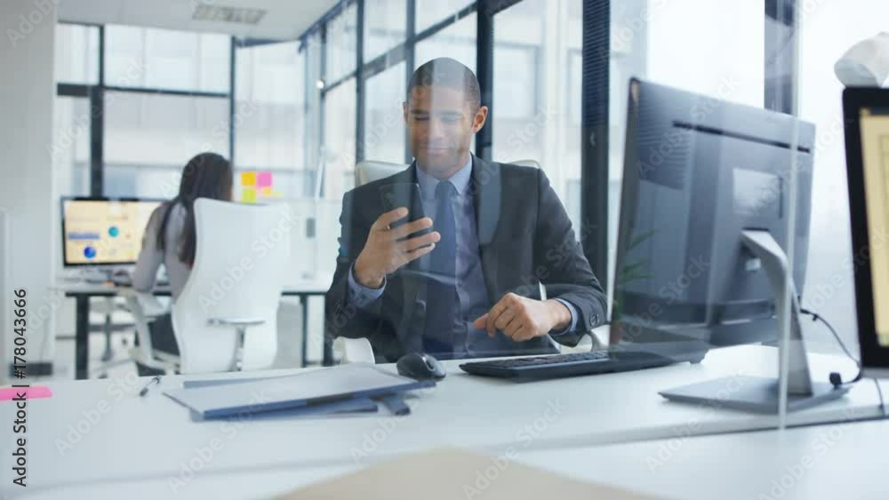Businessman working on computer in the office gets good news from phone call. Businessman working on computer in the office gets good news from phone call.