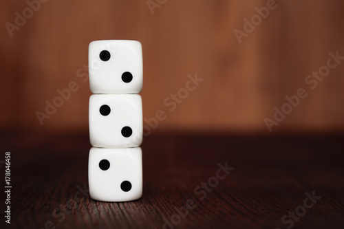 Three white plastic dices on each other on brown wooden board background. Six sides cube with black dots. Number 222.