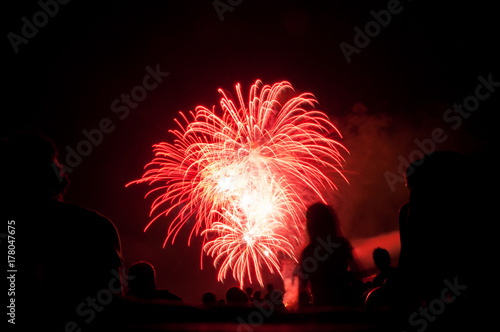 red fireworks with silhouettes of spectators  in foreground photo