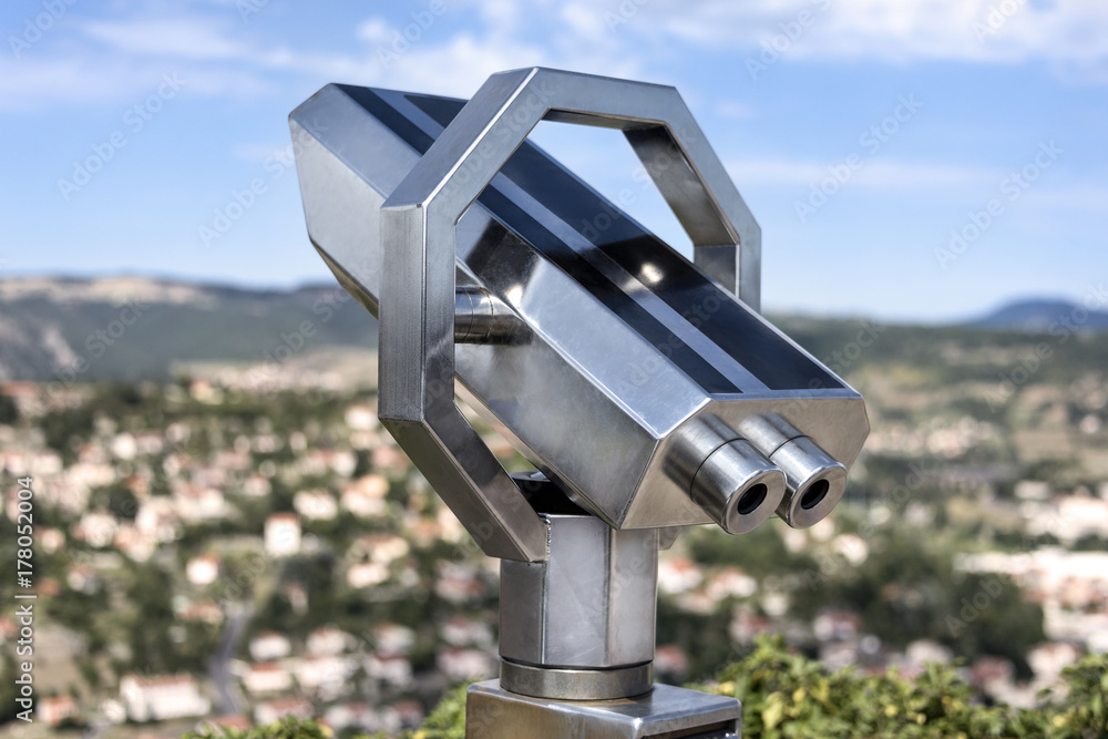 Silver metal touristic telescope on a viewing desk with blurred cityscape and horizon in the background Silver metal touristic telescope on a viewing desk with blurred cityscape and horizon in the background