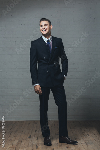A young man in a double breasted suit with his hand in his pocket laughing