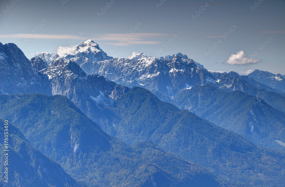 Snow-capped Mangart peak towering over forested ridges in the valley of Sava Dolinka river  in a sunny autumn day, Julian Alps, Triglav National Park, Slovenia, Europe