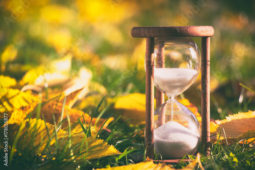 Hourglass in fallen leaves. Time is passing fast during autumn season. Time and season concept. 
