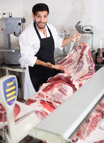 Happy butcher is demonstraiting meat to clients