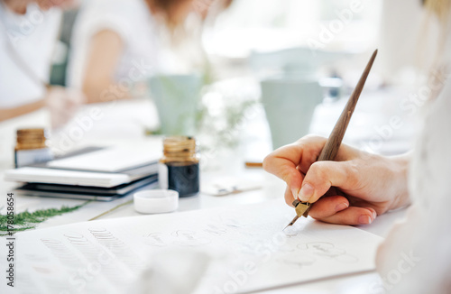 Training of calligraphy. The hand of a girl with a pen writes on paper with ink.