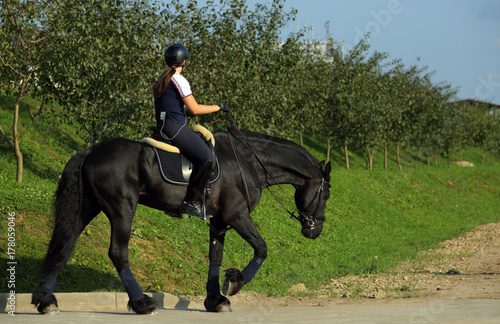Equestrian girl ride black friesian horse in summer park
