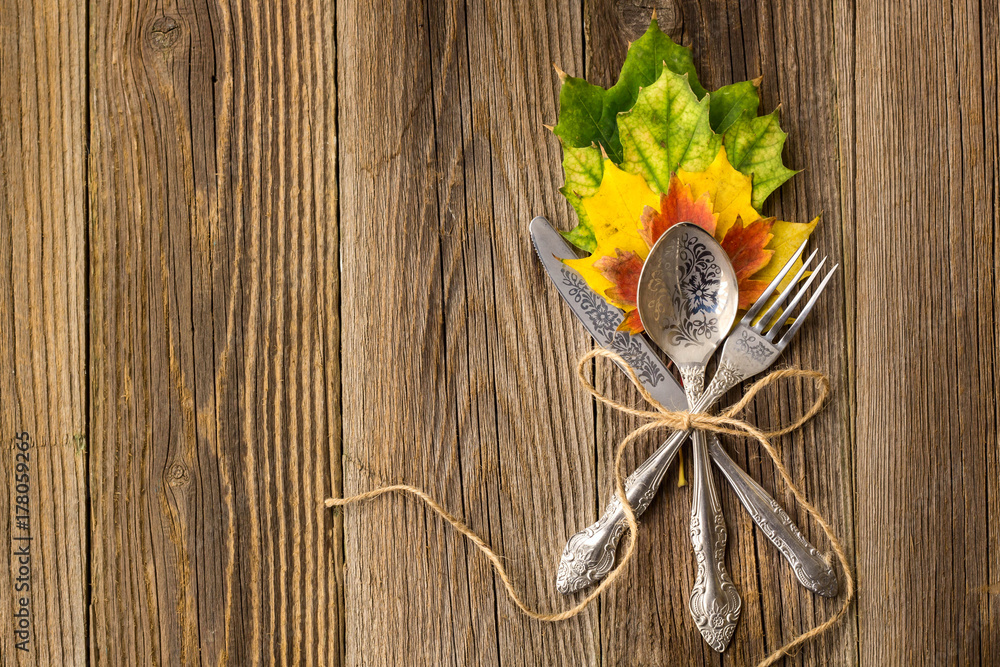 Autumn dinner place setting for Thanksgiving holiday with colorful maple leaves on rustic wooden boards Autumn dinner place setting for Thanksgiving holiday with colorful maple leaves on rustic wooden boards