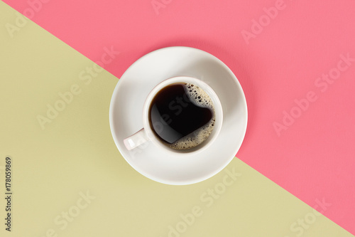 A cup of black coffee on pink and yellow background. View from above.