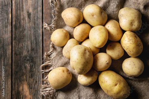 Raw whole washed organic potatoes on sackcloth over old wooden plank background. Top view with space