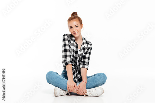 Cheerful ginger woman in shirt and jeans sitting on floor