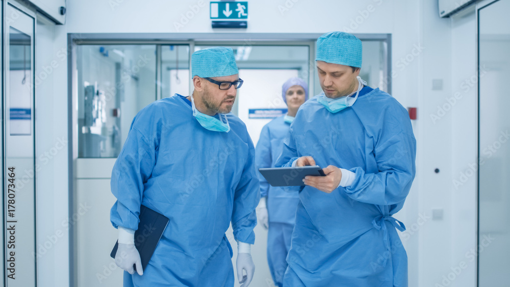 Two Doctors Walking through Hospital and having Discussion. One Holds Tablet in Hands. Two Doctors Walking through Hospital and having Discussion. One Holds Tablet in Hands.