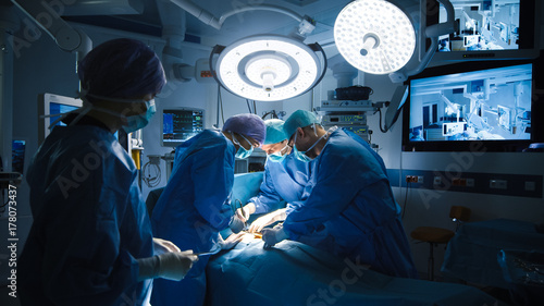Medical Team Performing Surgical Operation in Modern Operating Room. Dark Ambient. photo