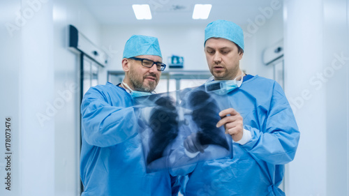 Two Doctors Walking Through Hospital and Discussing X-rayPhotograph Hold in Hands.