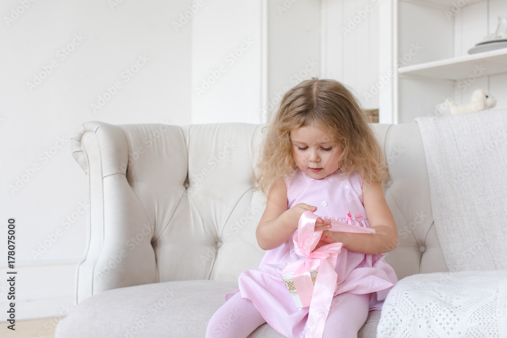 Adorable little toddler girl sitting on sofa with pink ribbon. Adorable little toddler girl sitting on sofa with pink ribbon.