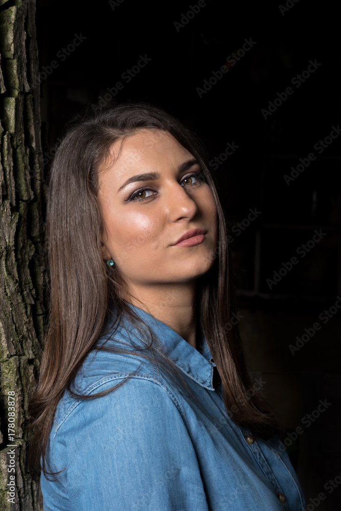 Fototapeta premium Beautiful smiling young girl leaning against a tree with copy space on black background