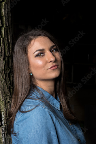 Beautiful smiling young girl leaning against a tree with copy space on black background