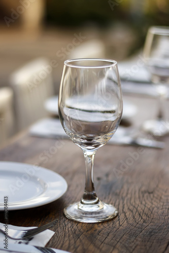 Empty wine glass stands on a wooden table next to a plate and a fork with a blurred background