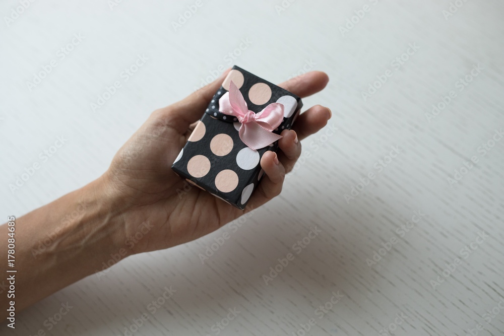 A gift is ready to be given to a person. Hands are holding a small box wrapped with a nice paper with surprise. Concept of season gifts, appreciation and love, friendship and happiness, style..