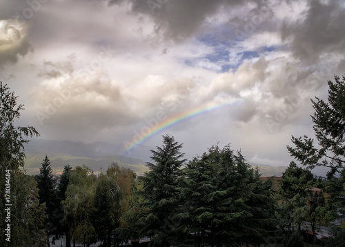 Fantastical Atmospheric Mountainous Landscape with Central Rainbow in Stormy Cloudy Sky