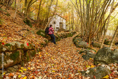 Piedicavallo, Italy - October 20, 2017: Young man observes the old rustic house along an alpine trail full of autumn colors