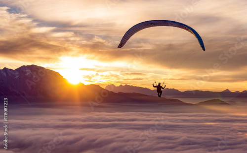 An adventurous sportsman does paragliding above the clouds at sunset. photo