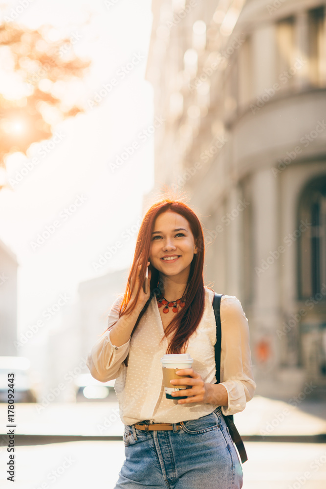 Young woman with coffee to go standing at the street and using mobile phone  