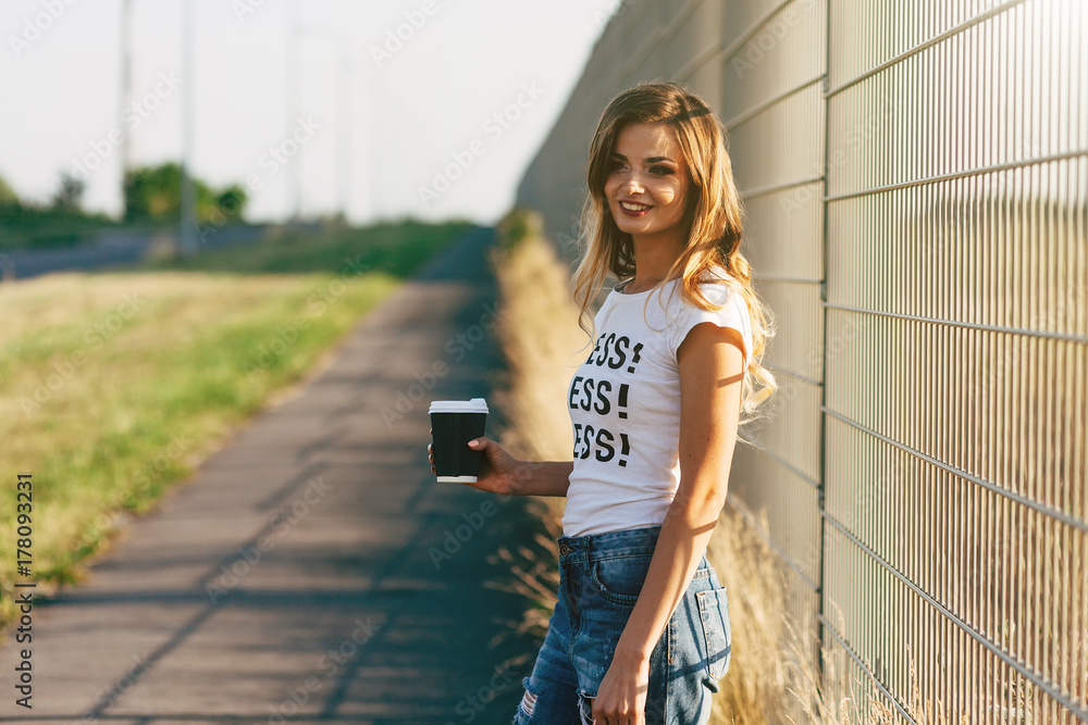 Beautiful woman walking with coffee and shopping bag in white T-shirt with word 