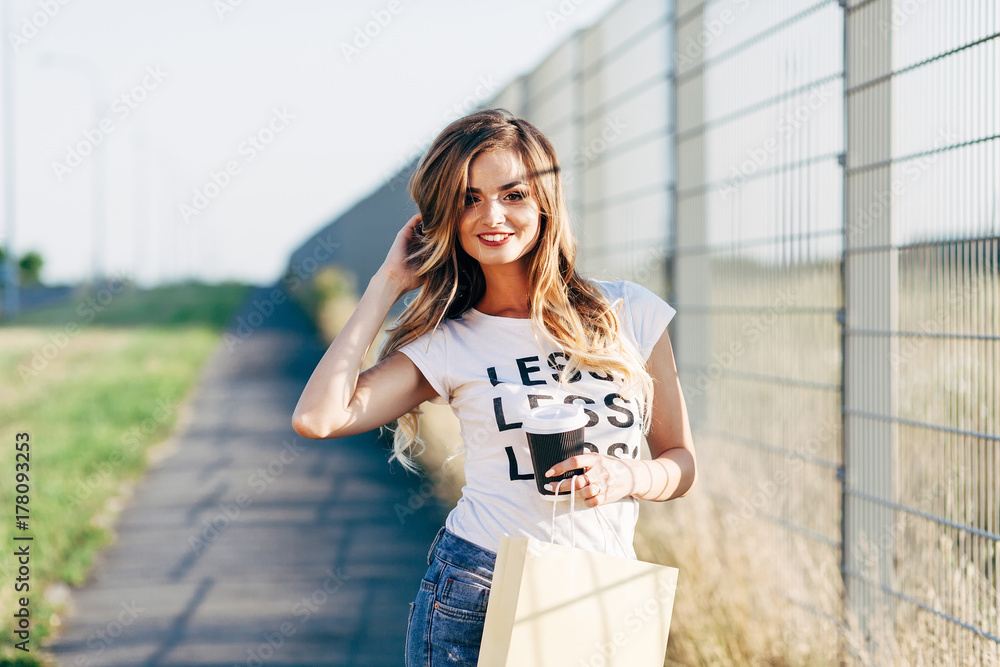 Beautiful woman walking with coffee and shopping bag in white T-shirt with word 