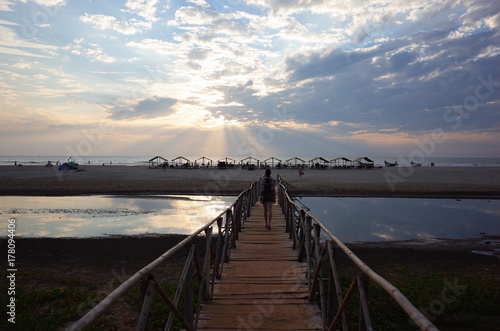 the girl goes off into the distance to the sunset ocean and the beach along a long wooden bridge