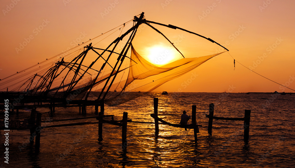Indian man fishing under the great Chinese nets at Cochin, Kerela, India.