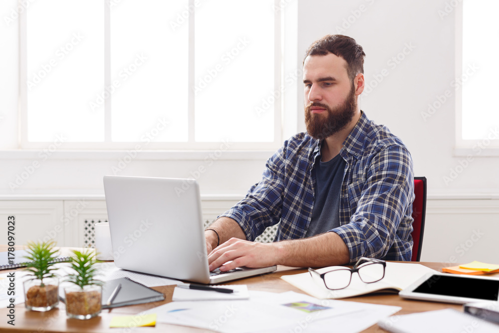 Young concentrated businessman with laptop in modern white office Young concentrated businessman with laptop in modern white office