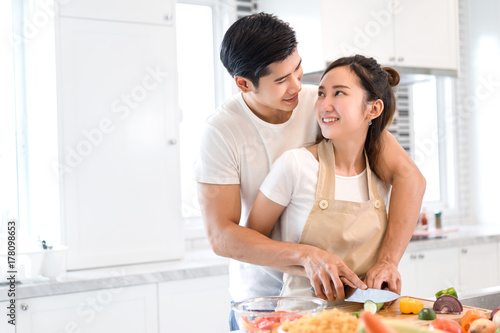 Couple cooking food in kitchen room, Young Asian man and woman together cutting slice vegetables making each salad for dinner menu with fruits at home romantic indoor sweet lover, copy space the left.