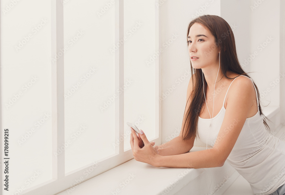 Young pensive woman in headphones at window Young pensive woman in headphones at window