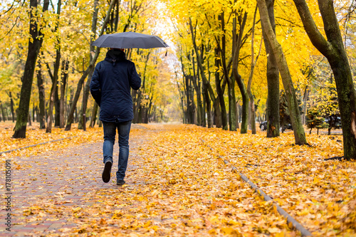 a man with an umbrella walking along the autumn park