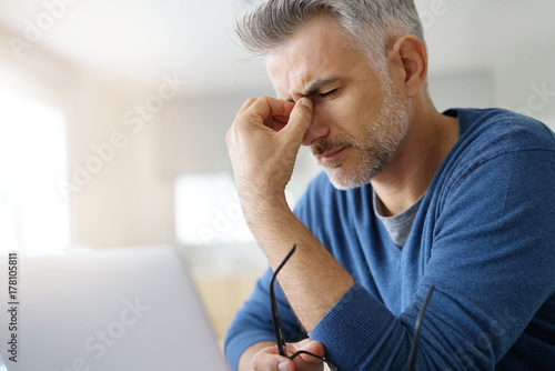 Man at home having a headache in front of laptop