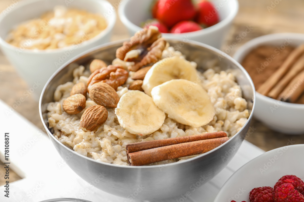 Tasty oatmeal with banana, nuts and cinnamon in bowl on table